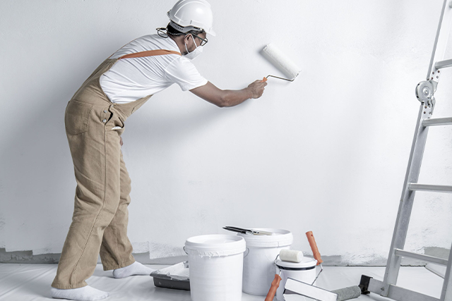 Painter Wearing Overalls and Helmet Painting White Wall Indoors