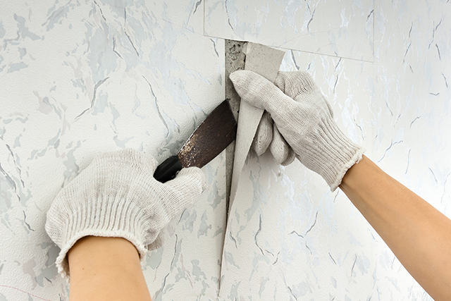 Hands in Gloves Removing Wallpaper with Scraper for Home Improvement
