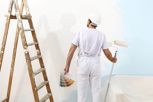 Painter Holding Color Samples and Roller Near Ladder in a Room