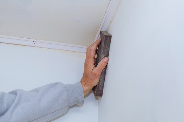 Person Sanding Drywall Ceiling During Home Improvement Project