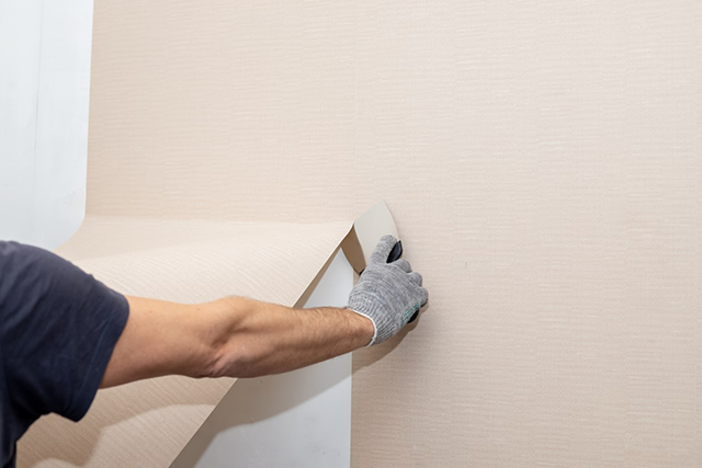Person Removing Wallpaper with Gloved Hand, Home Improvement Service